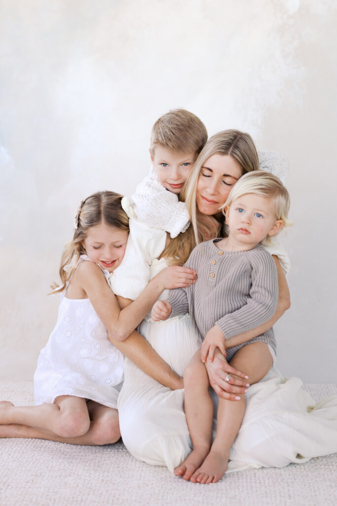 pregnant mom snuggles with her 3 older kids in a beautiful minneapolis studio for her minneapolis matenrity photoshoot