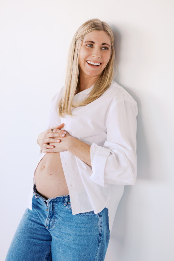 what to wear for maternity photos - woman in white button down and jeans with pregnant belly showing.