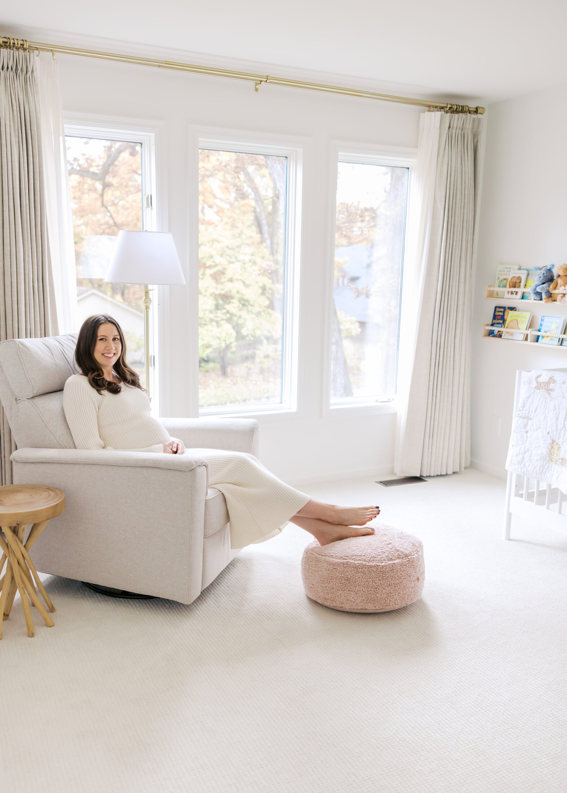 woman in long white sweater dress sits on a chair in her baby's nursery for her minnetonka in-home maternity photography session