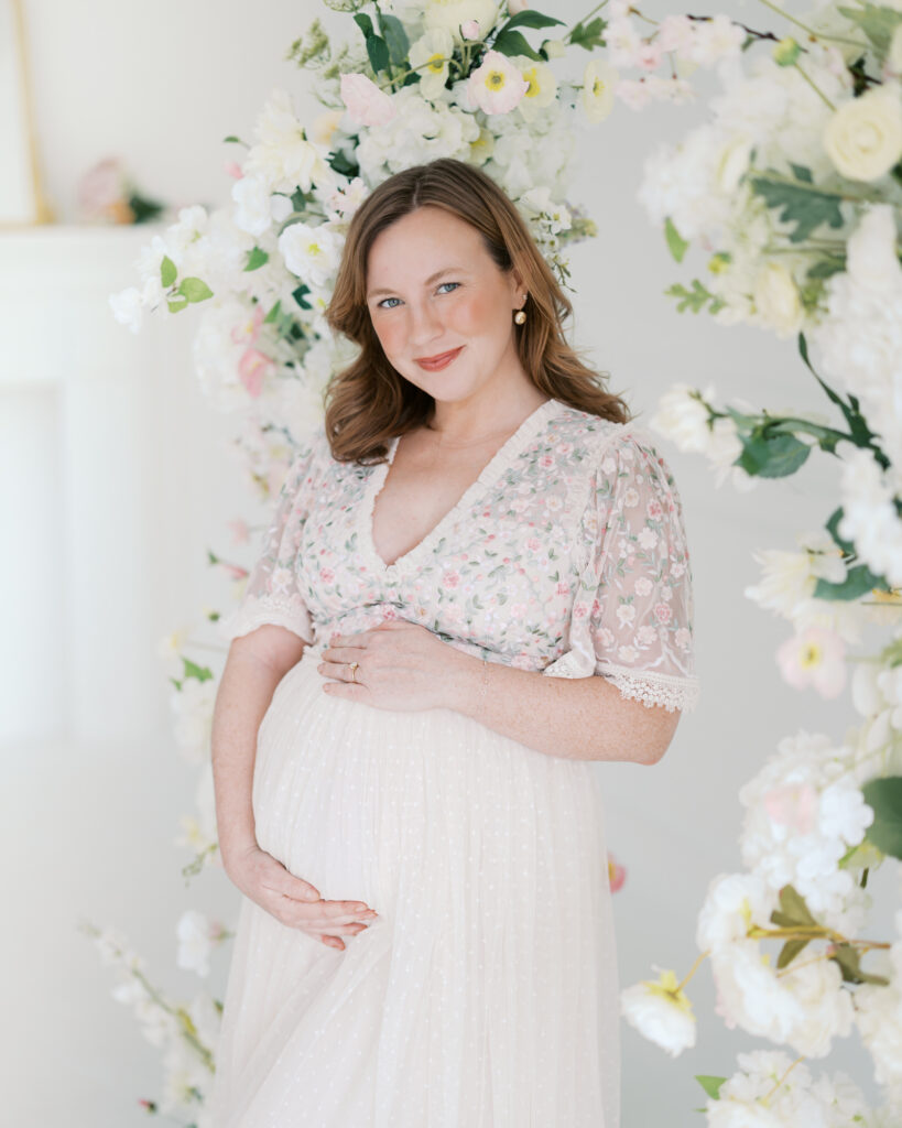 pregnant woman is surrounded by flowers in a studio setting for her minneapolis maternity photoshoot