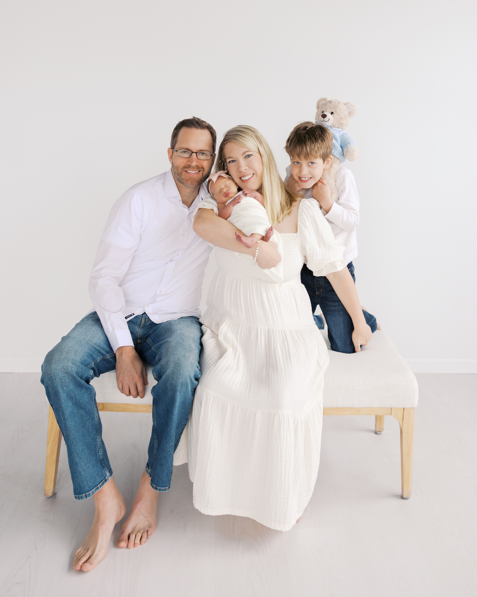Family of four sitting on a bench during their minneapolis studio photography session with angela watts.