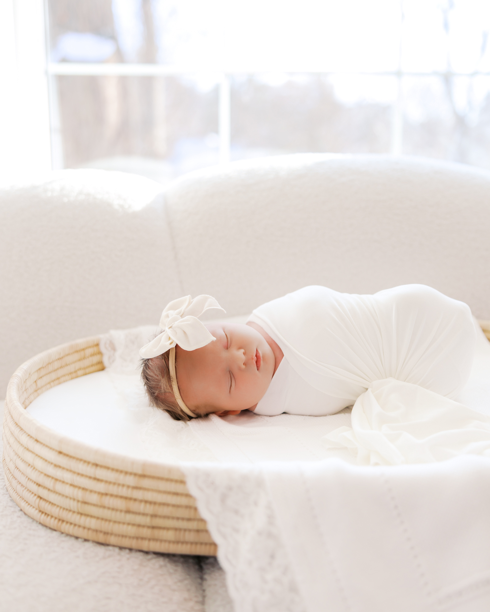 Baby girl with white bow lays in a changing basket during her peaceful in-studio newborn photography session with angela watts photography
