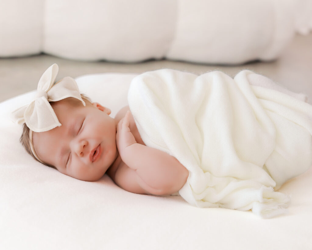 Newborn baby sleeps on white blanket during her newborn photography session in a light-filled  minneapolis studio.