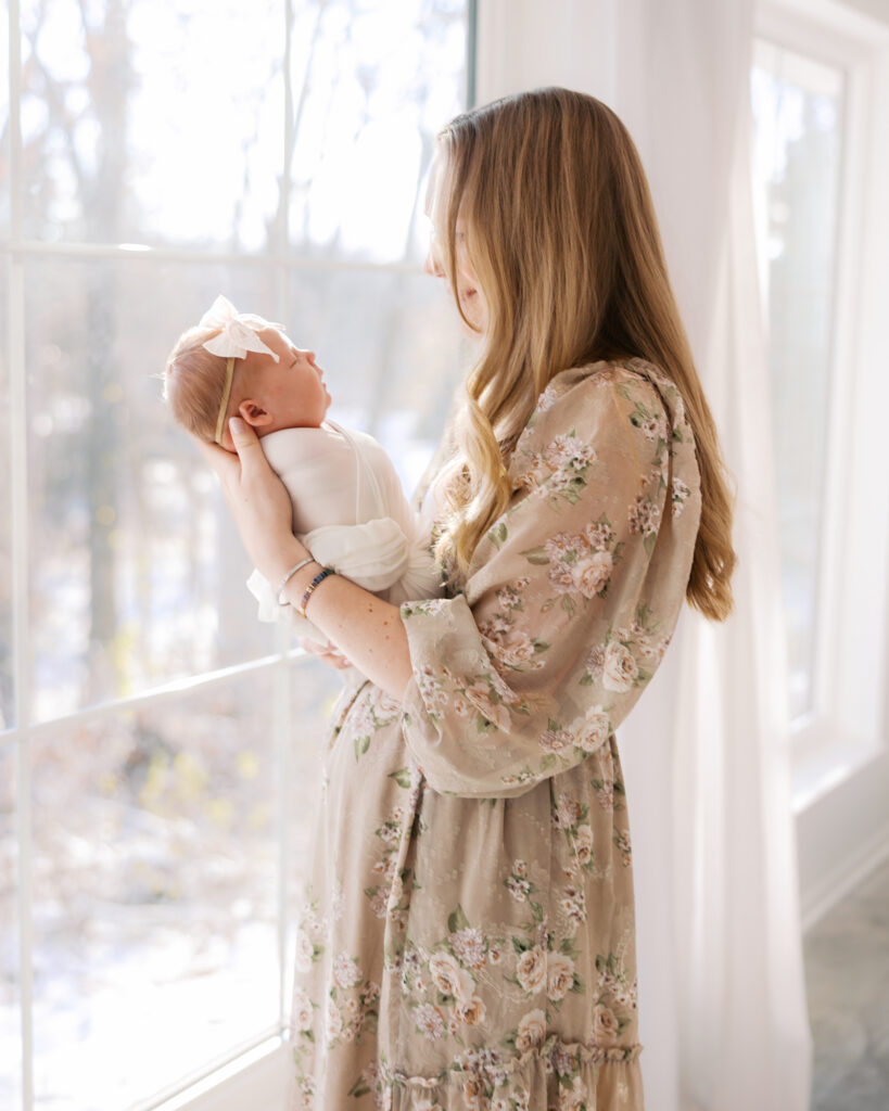 Mom and newborn baby cuddle peacefully by a window during their studio newborn photography session with angela watts photography