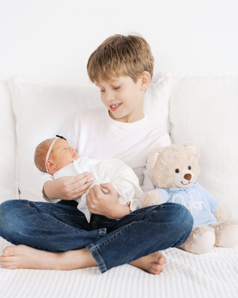 Big brother holds his baby sister for the very first time during their minneapolis studio maternity photoshoot with angela watts photography.