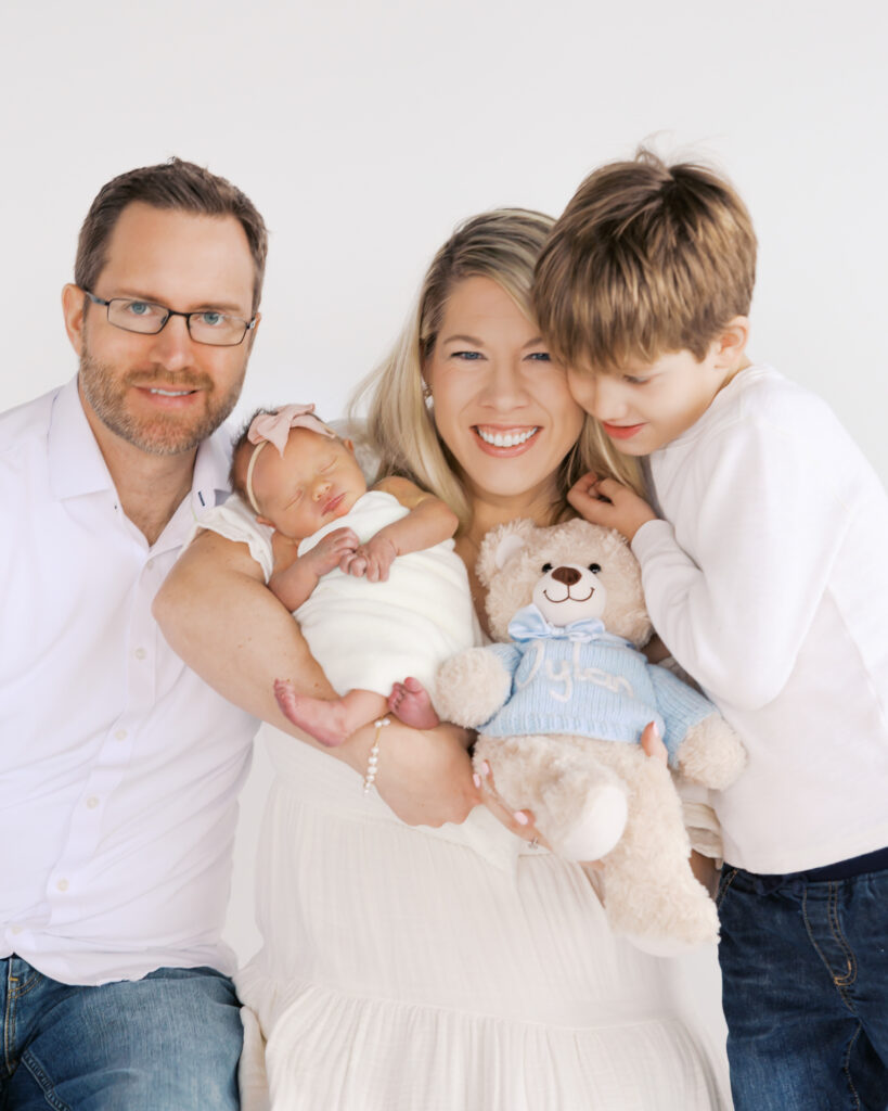 Family of four cuddles with big smiles during their newborn photo session in a light-filled studio.
