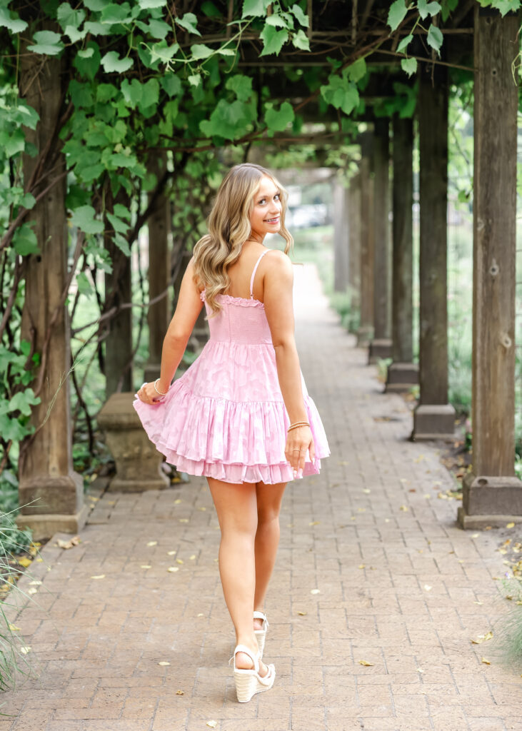 Girl in short pink dress walks through Noerenburg Gardens for her Wayzata senior pictures with angela watts photography