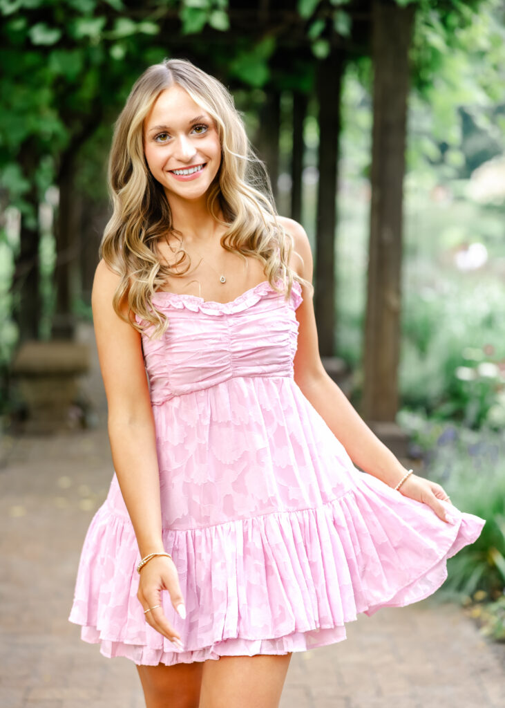 Girl in short pink dress walks through Noerenburg Gardens for her Wayzata senior pictures with angela watts photography