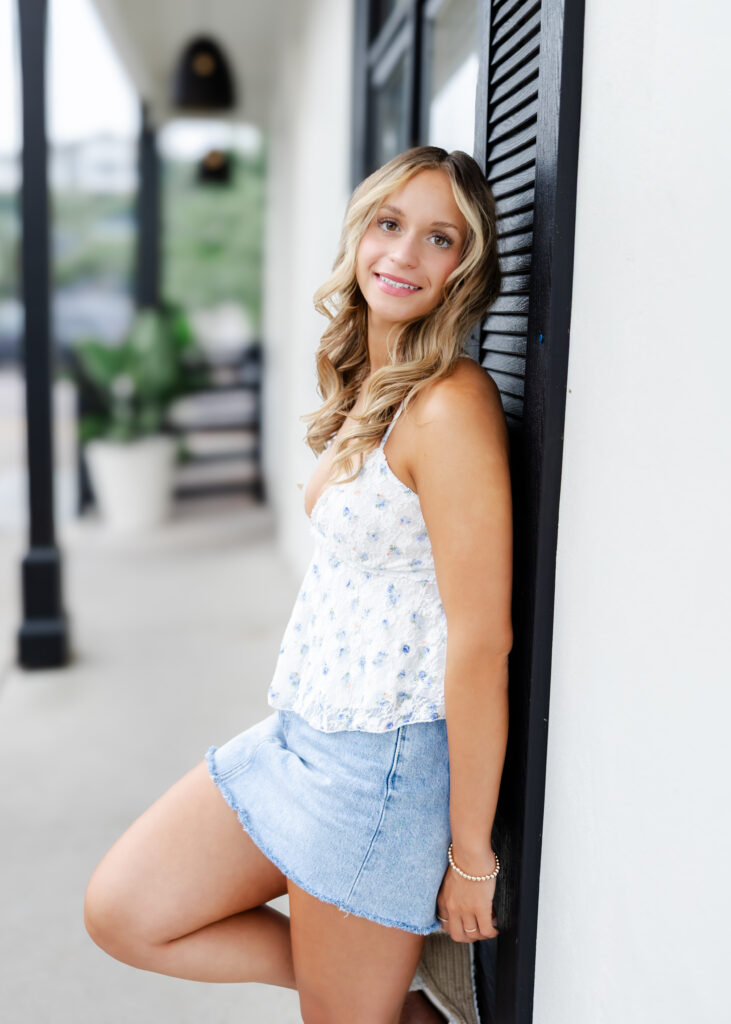 Girl in white tank and denim skirt poses downtown Wayzata for her wayzata senior pictures with angela watts photography