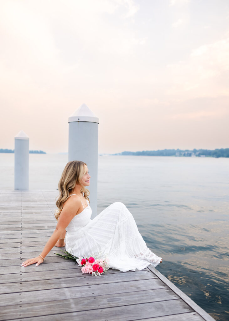Girl in long white dress poses on the docks of Wayzata for her wayzata senior pictures with angela watts photography