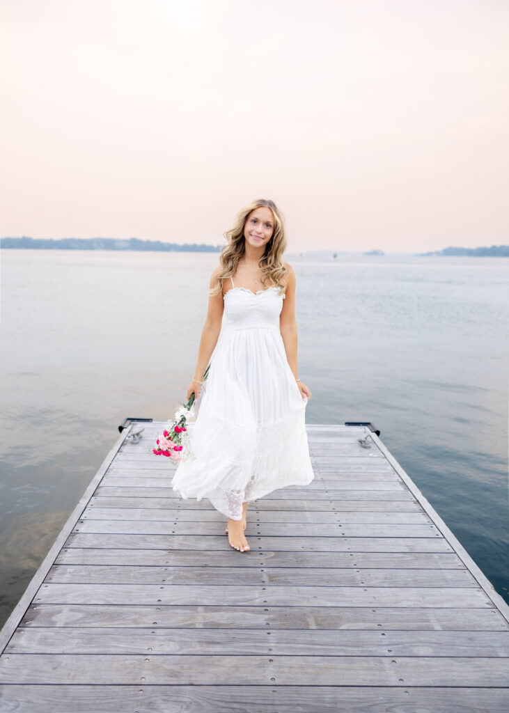 Girl in long white dress poses on the docks of Wayzata for her wayzata senior pictures with angela watts photography