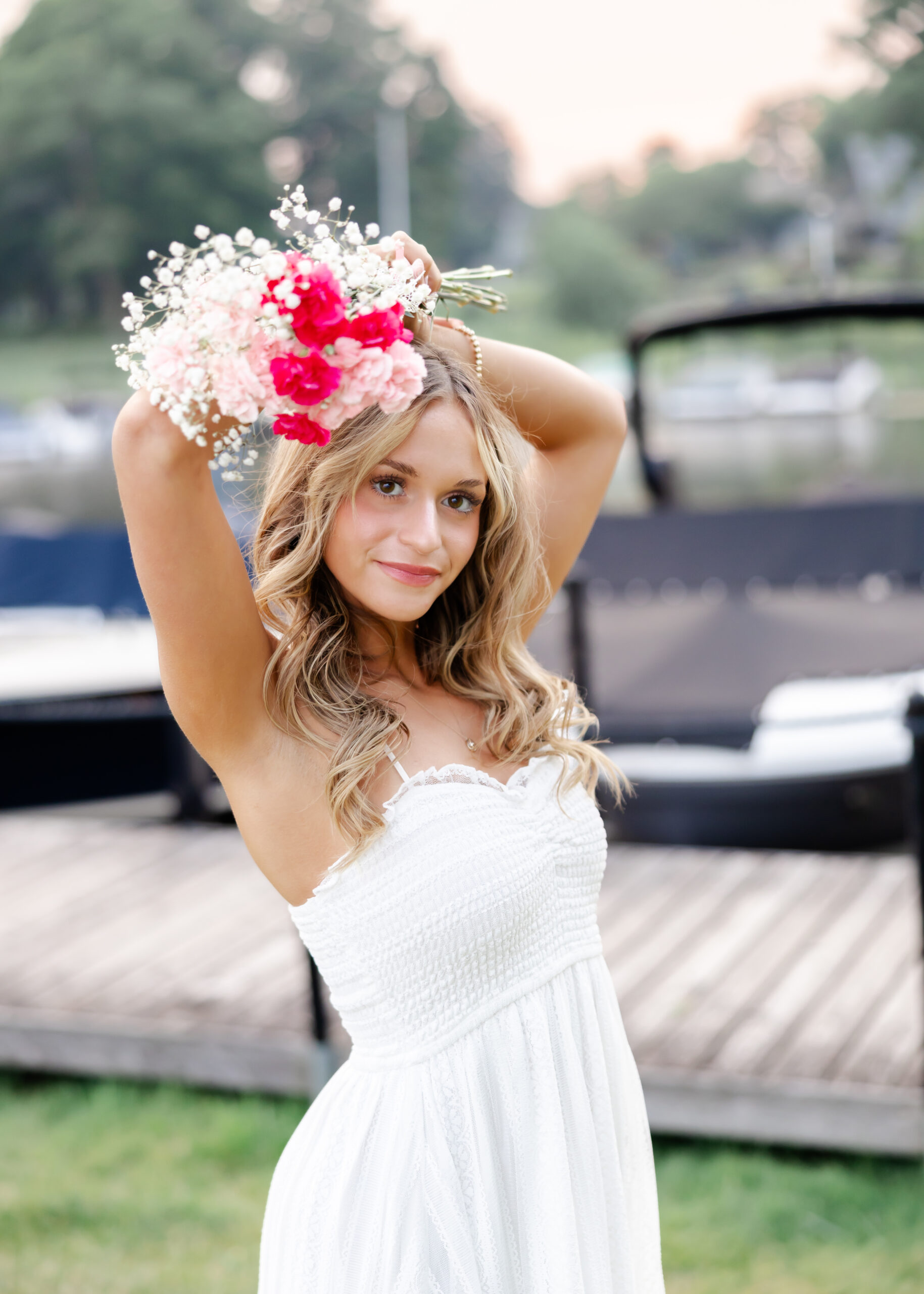 Girl in long white dress poses at wayzata beach for her wayzata senior pictures with angela watts photography