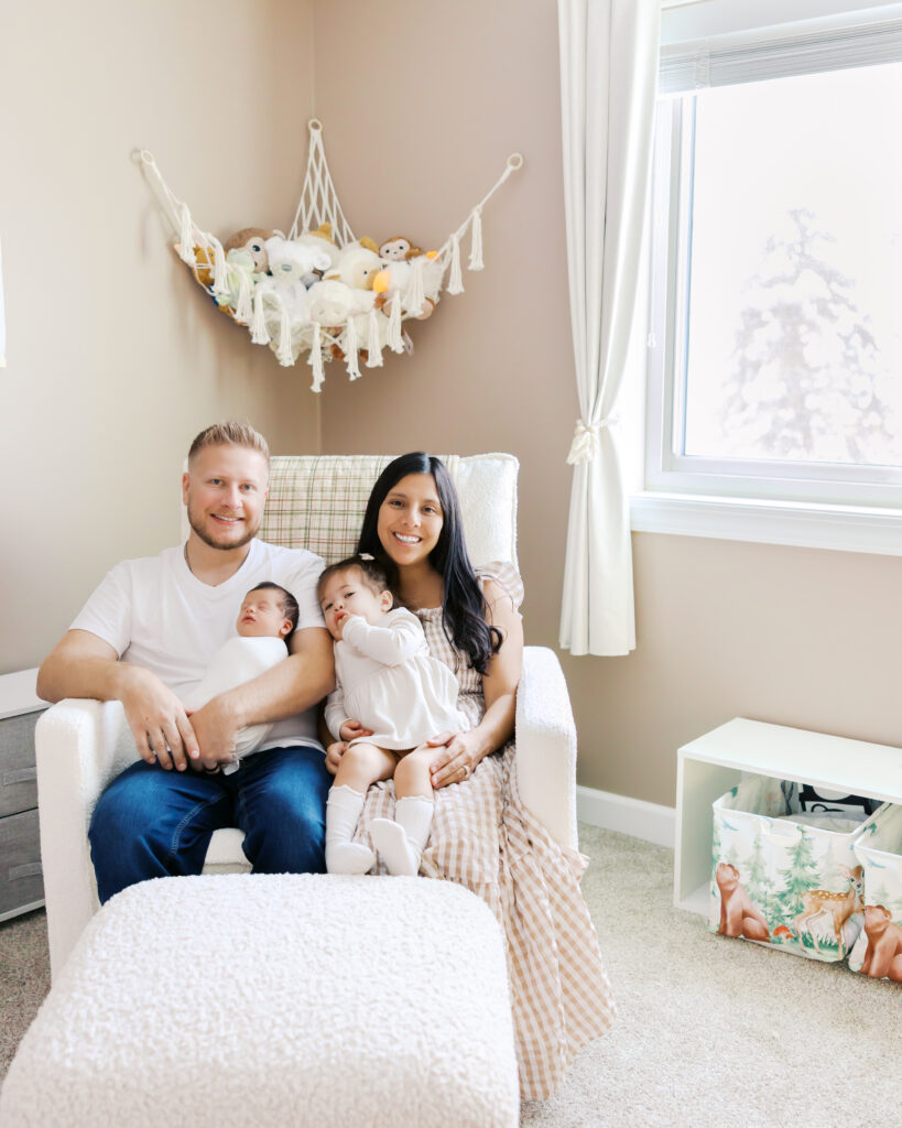 Family of four snuggle in their in-home nursery during their minneapolis newborn photography session with angela watts photography