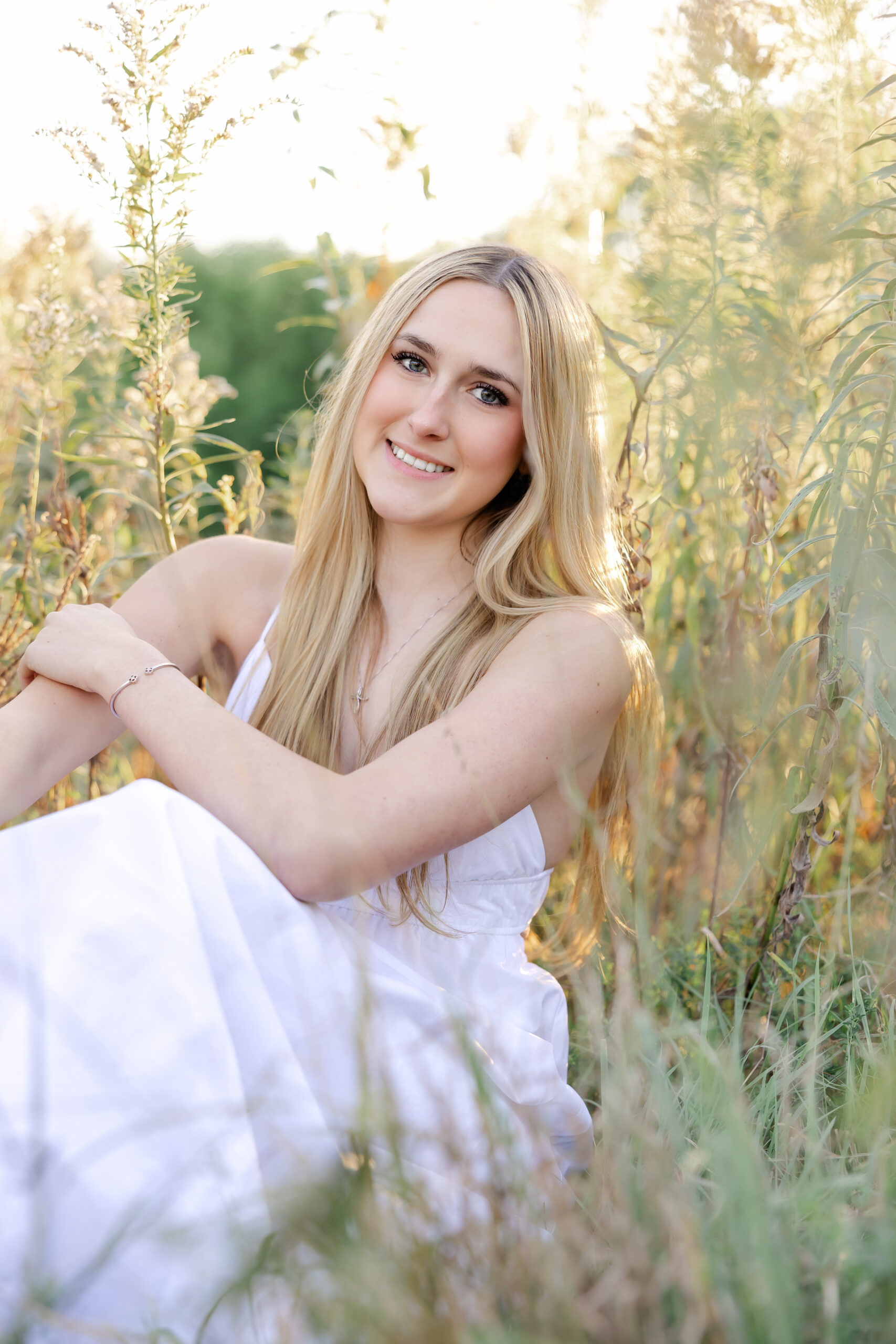 girl in long white dress poses at golden hour for her wayzata senior portraits