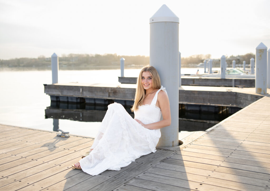 Girl in white dress sits on wayzata doc for her minneapolis senior photos with angela watts photography