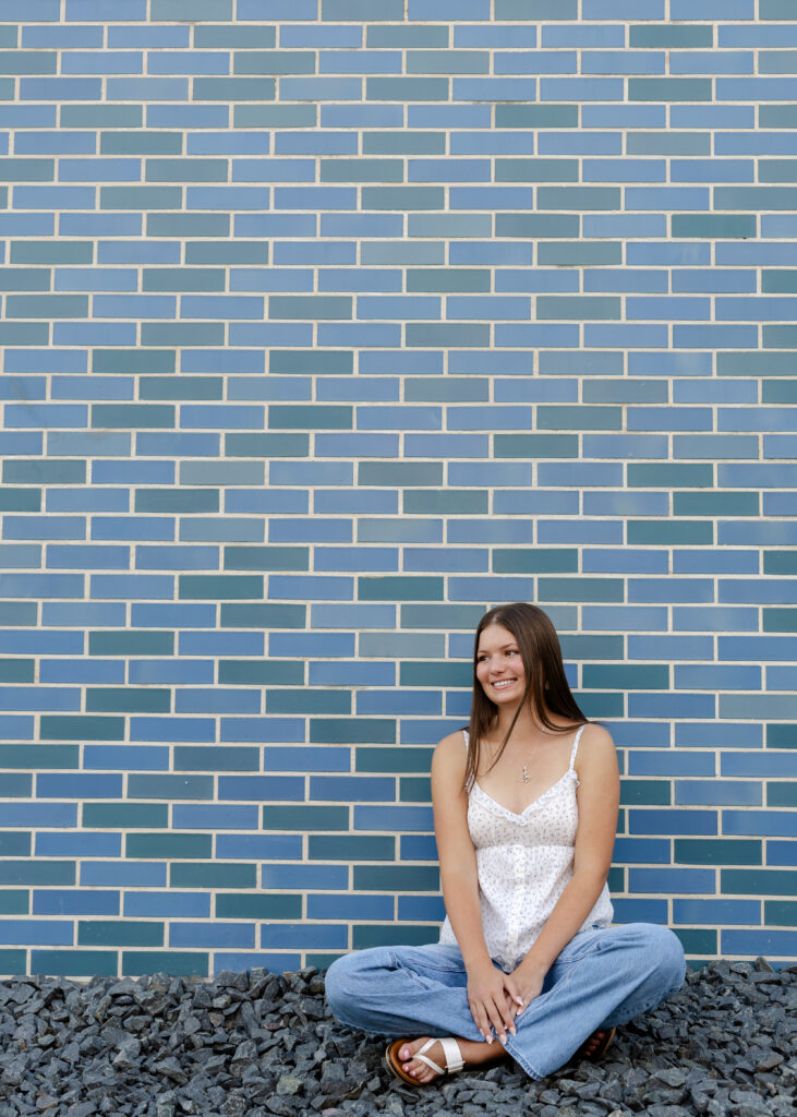 Girl poses in front of blue and green brick wall downtown excelsior for her eden prairie senior pictures with angela watts photography