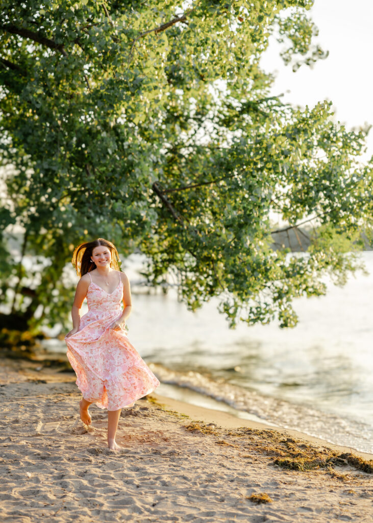 girl in long pink and white dress runs in the sand at wayzata beach for her minneapolis senior pictures photography session
