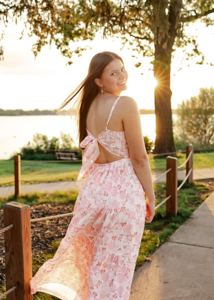 Girl poses at golden hour at excelsior beach in white and pink flowy dress for her eden prairie senior pictures with senior photographer angela watts photography.