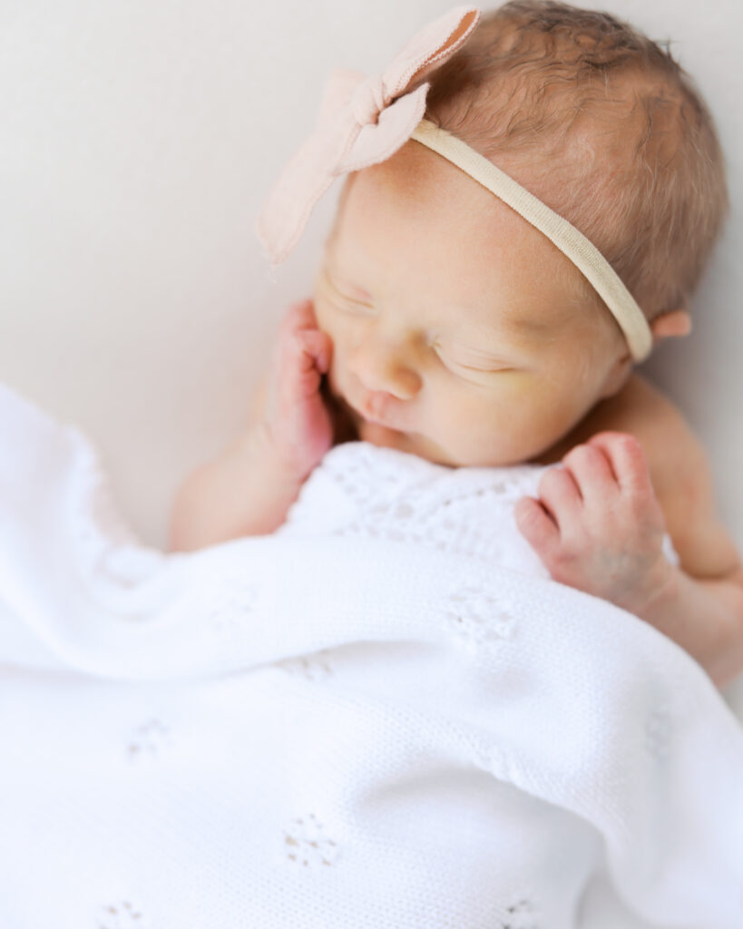 baby girl in pink bow sleeps in white blanket during her minneapolis newborn photos with newborn photographer angela watts.