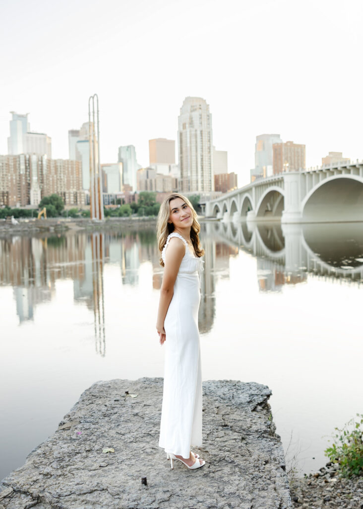 Wayzata high school senior in long white dress poses at st anthony  main for her wayzata senior pictures with angela watts photography