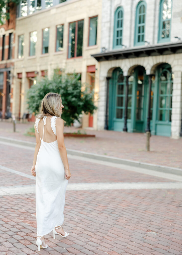 Wayzata high school senior in long white dress poses at st anthony  main for her wayzata senior pictures with angela watts photography