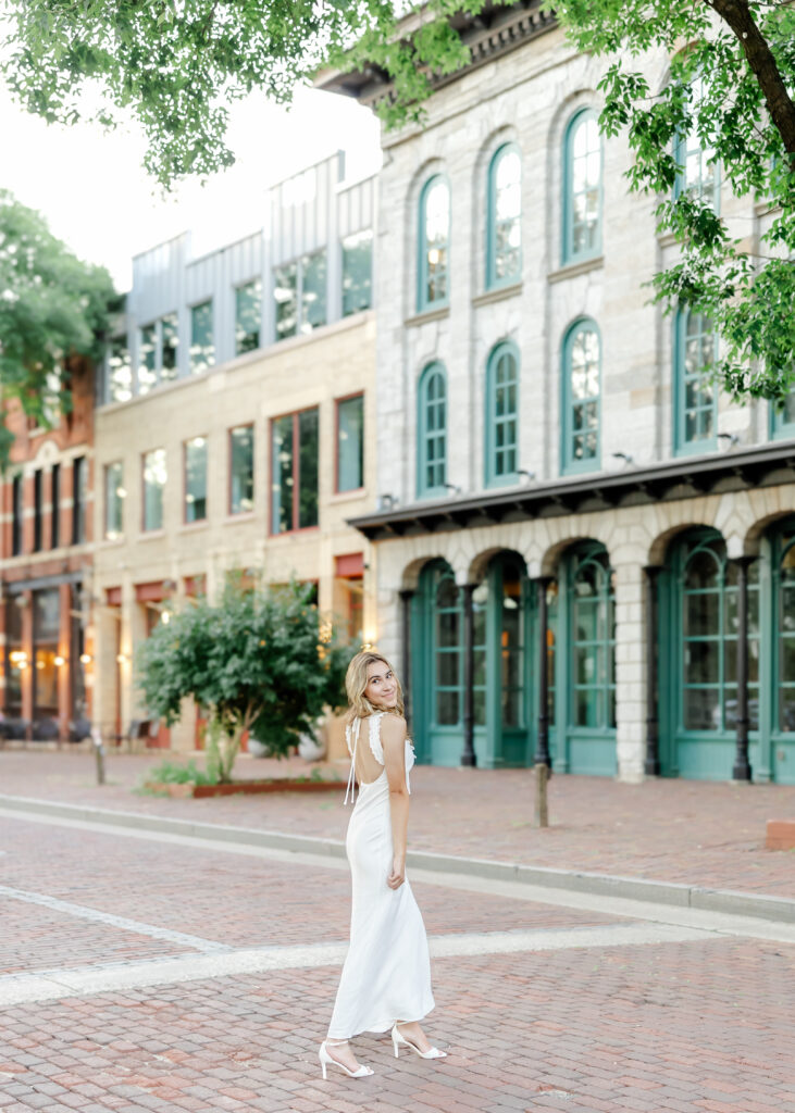 Wayzata high school senior in long white dress poses at st anthony  main for her wayzata senior pictures with angela watts photography