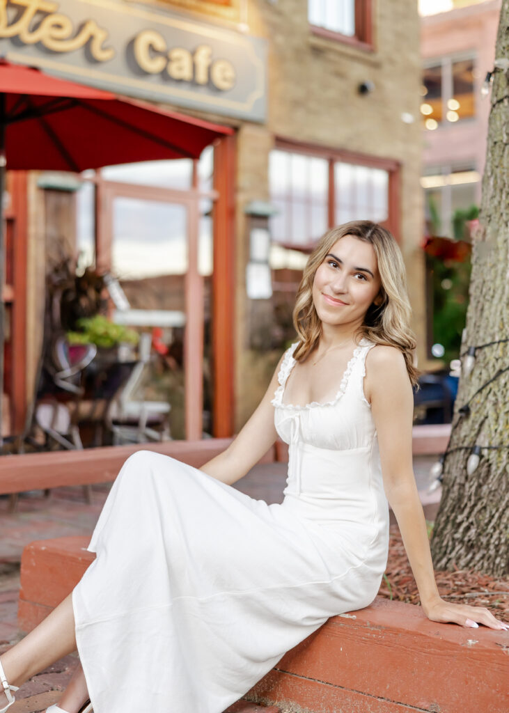 Wayzata high school senior in long white dress poses at st anthony  main for her wayzata senior pictures with angela watts photography