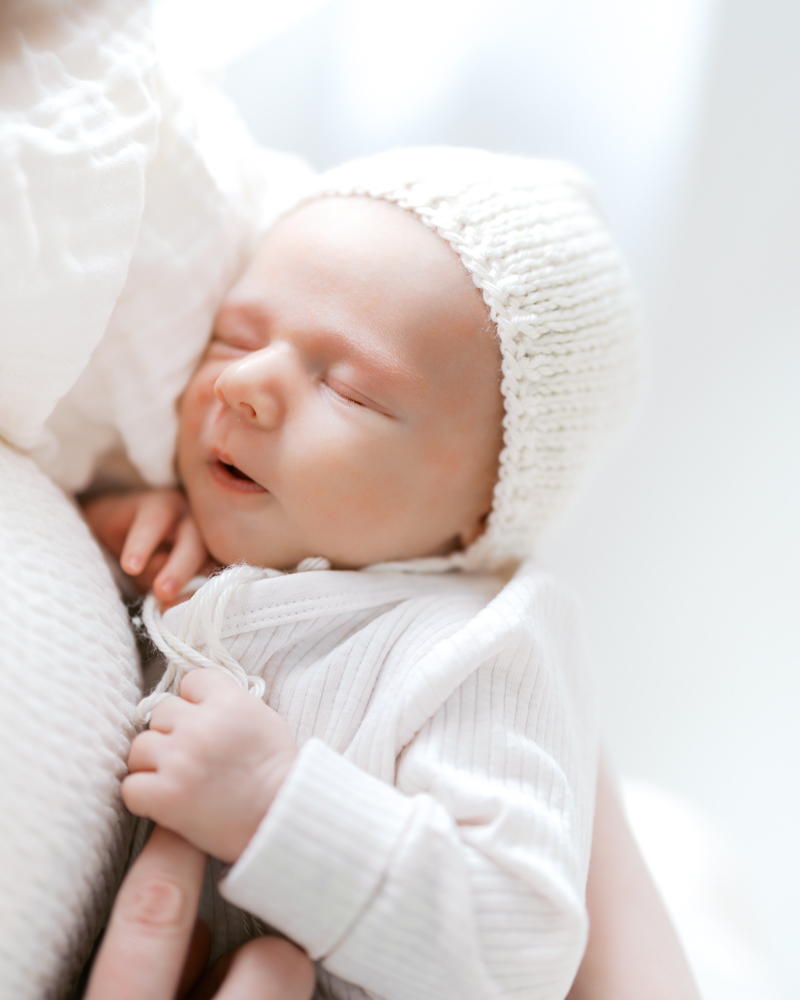 baby boy wearing hand-knit bonnet sleeps in moms arms during his minneapolis newborn photography session