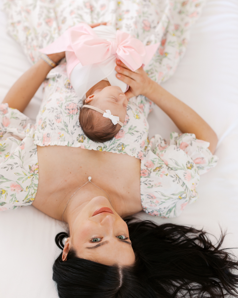 Woman lies on a white bed holding her newborn baby girl during their wayzata newborn photography session with angela watts photography