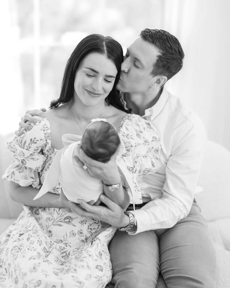 Black and white image of dad kissing mom on the cheek while mom holds newborn baby girl during their minneapolis newborn photography session.