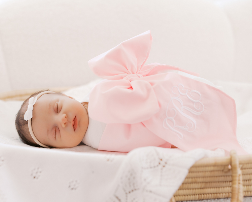 Newborn baby girl swaddled and wrapped in a big pink bow sleeps in changing basket for her wayzata newborn photography session with angela watts photography.