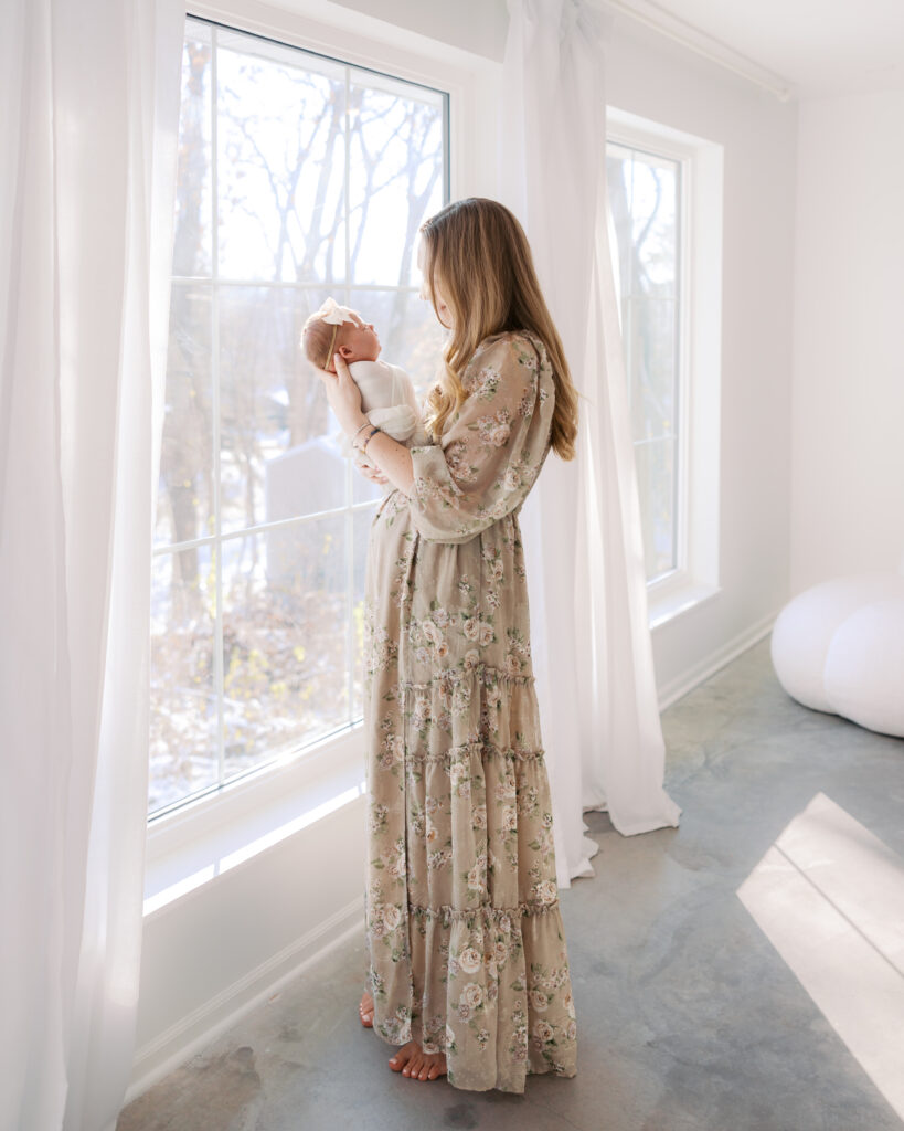 Mom holds newborn baby in a light-filled studio during their edina newborn photography session with angela watts photography
