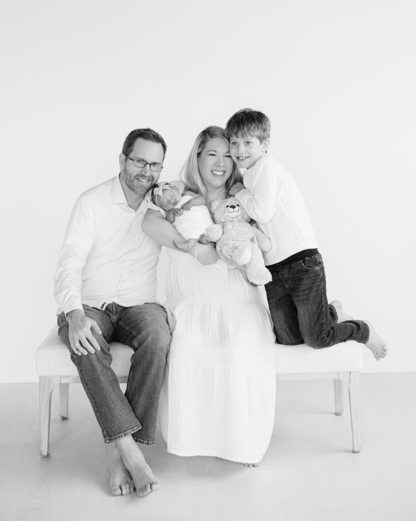 Family of four snuggle close on a bench during their minneapolis studio newborn photography session with angela watts photography