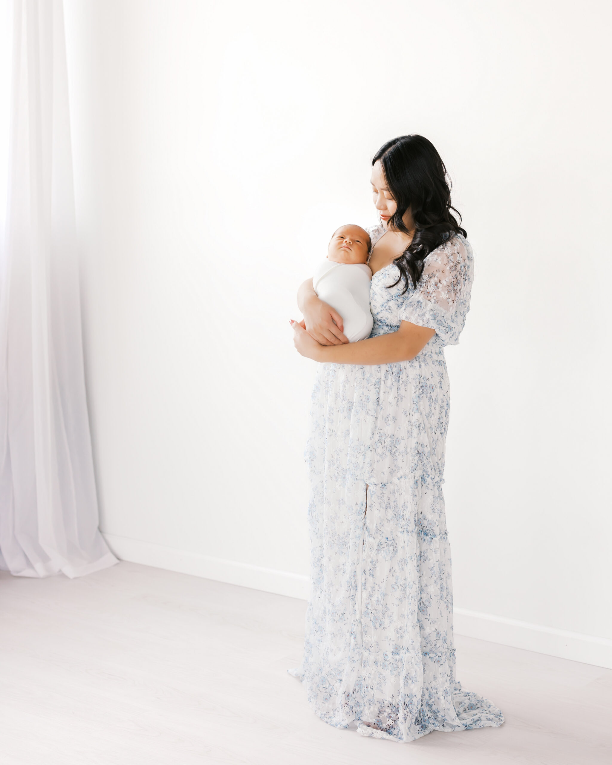 Woman in blue and white long dress holds her newborn baby during her minneapolis studio newborn photography session with angela watts photography