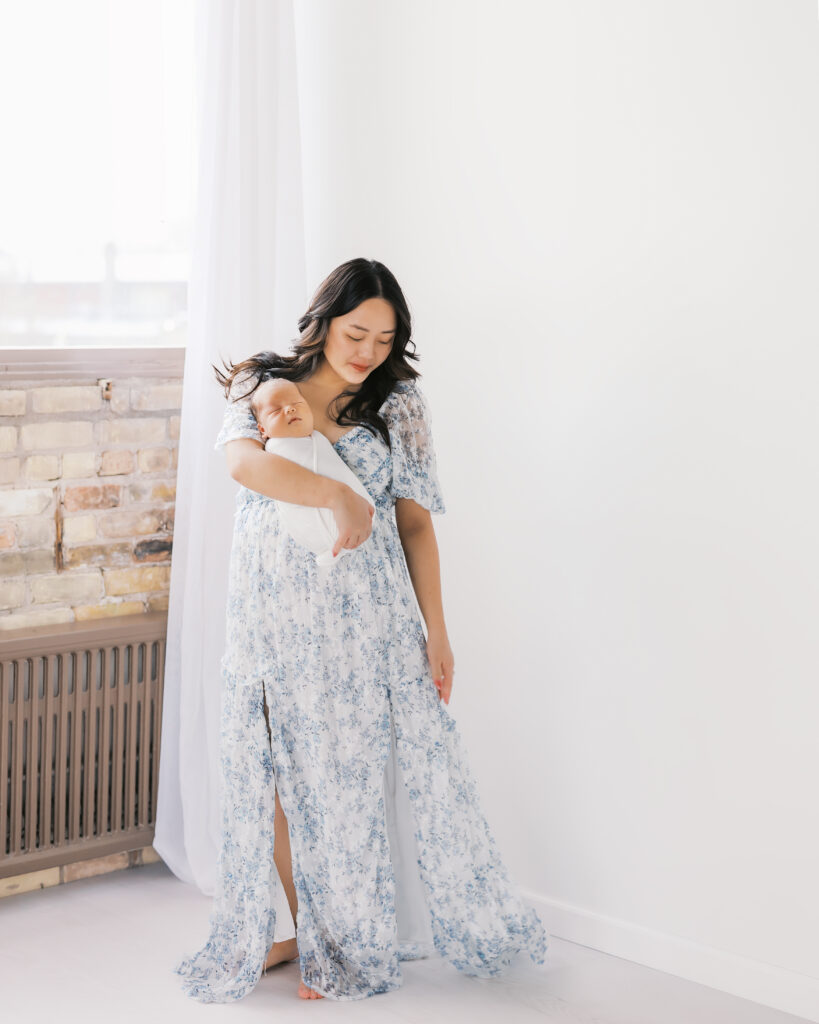 Mom in beautiful long blue dress holds newborn baby during their edina studio newborn photography session with angela watts photography