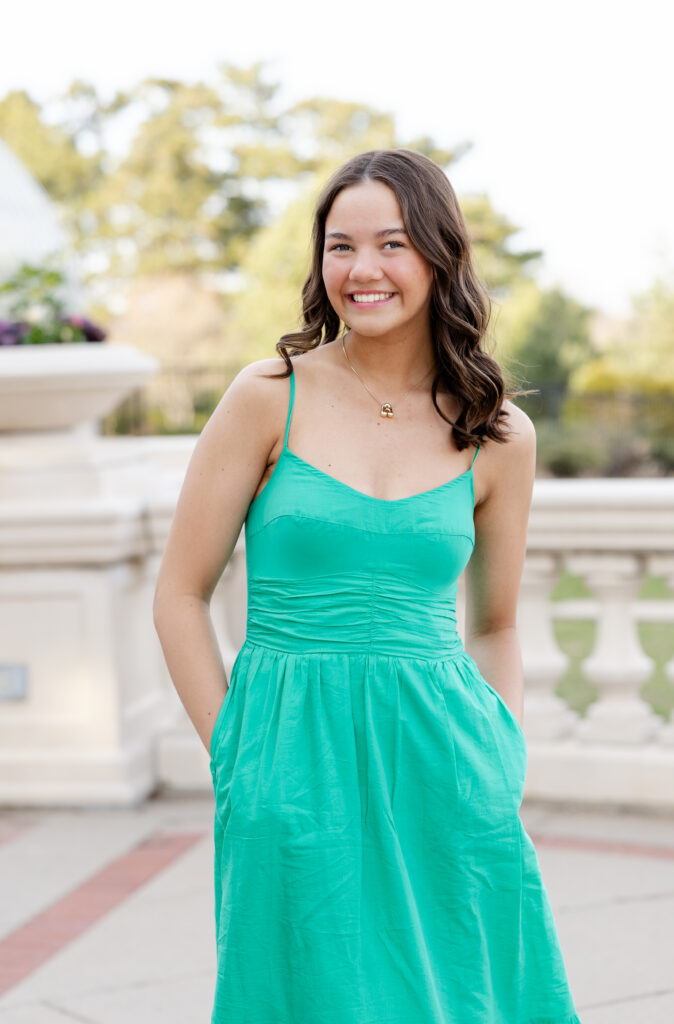 girl in long green dress poses at como park conservatory for her minneapolis senior pictures