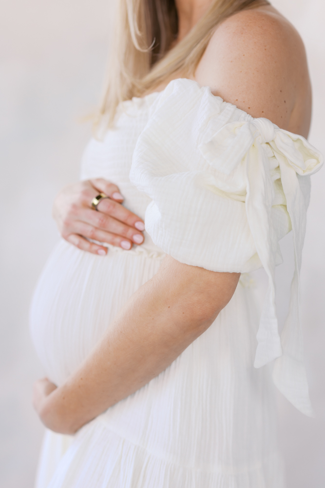 woman in light cream dress holds pregnant belly at minneapolis studio during her maternity photography session
