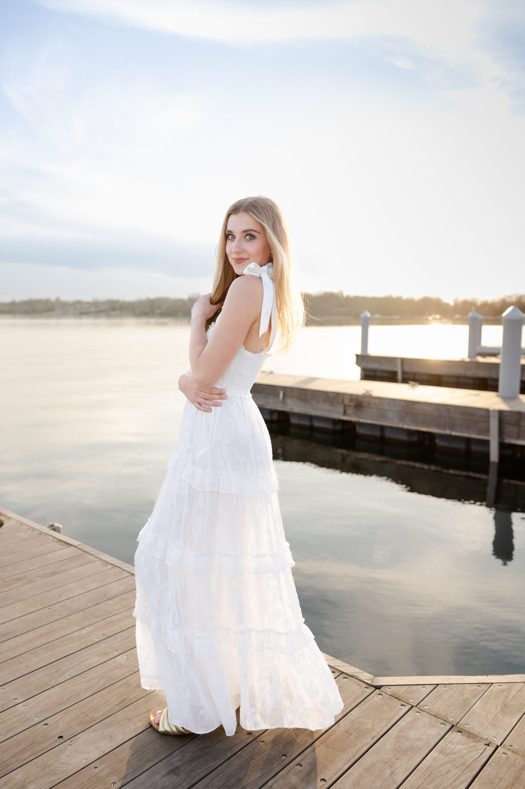 girl in long white dress poses on wayzata dock for her minneapolis senior pictures photography session