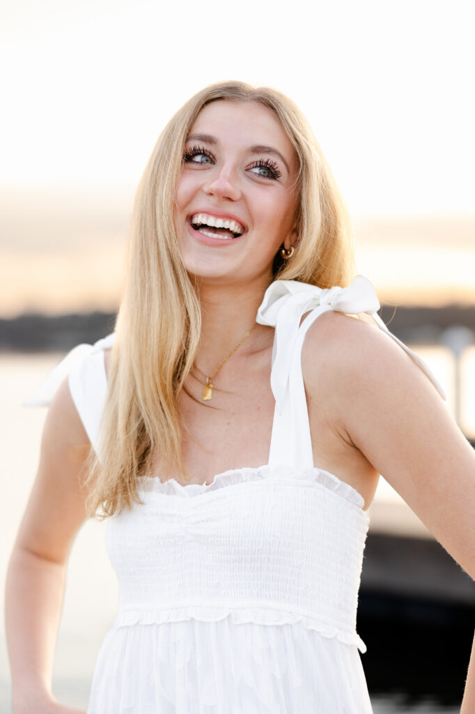 girl in white dress laughs past the camera on the docks downtown wayzata for her wayzata senior pictures