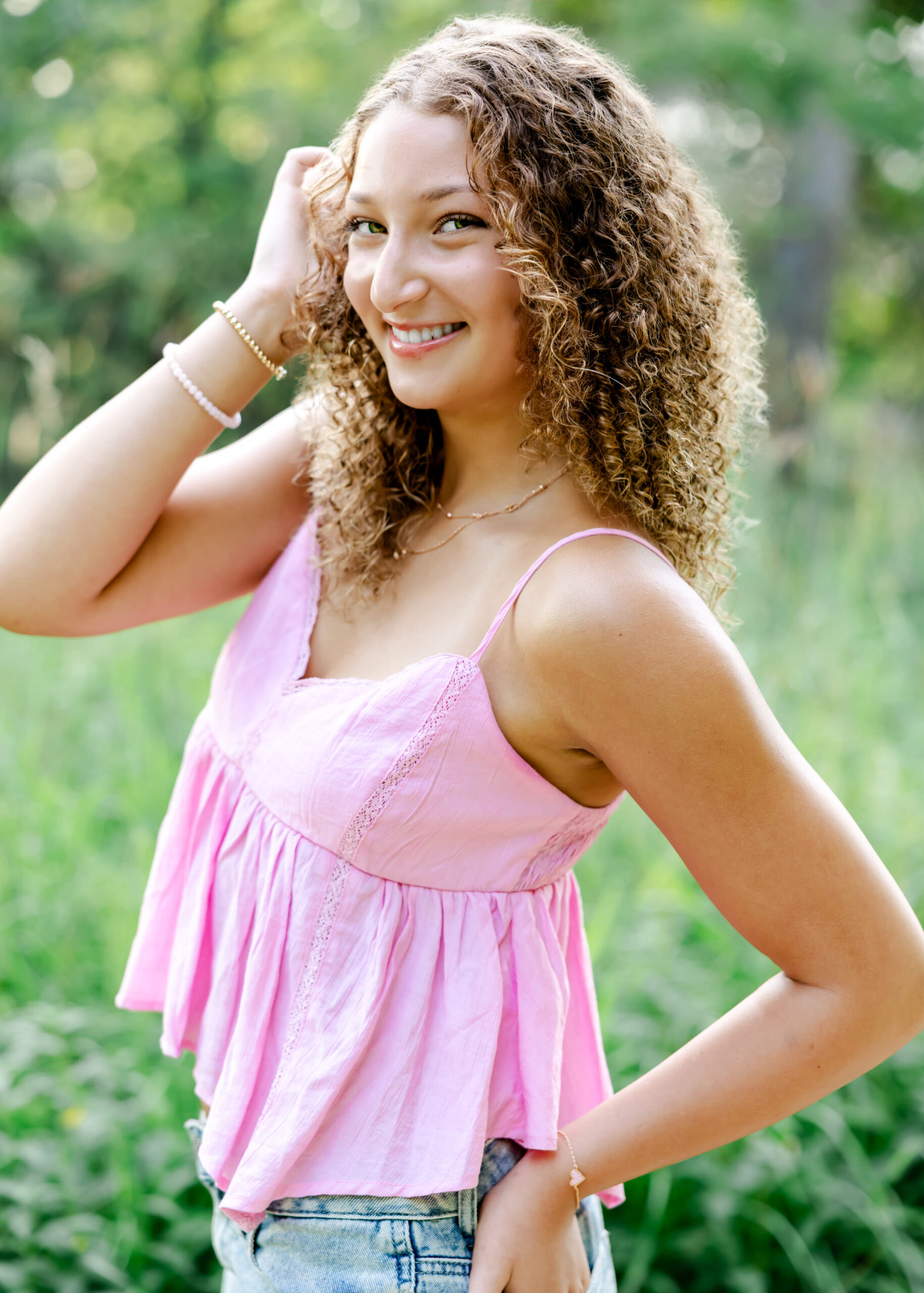 girl wearing pink tank and jeans surrounded by greenery poses for her minneapolis senior pictures session