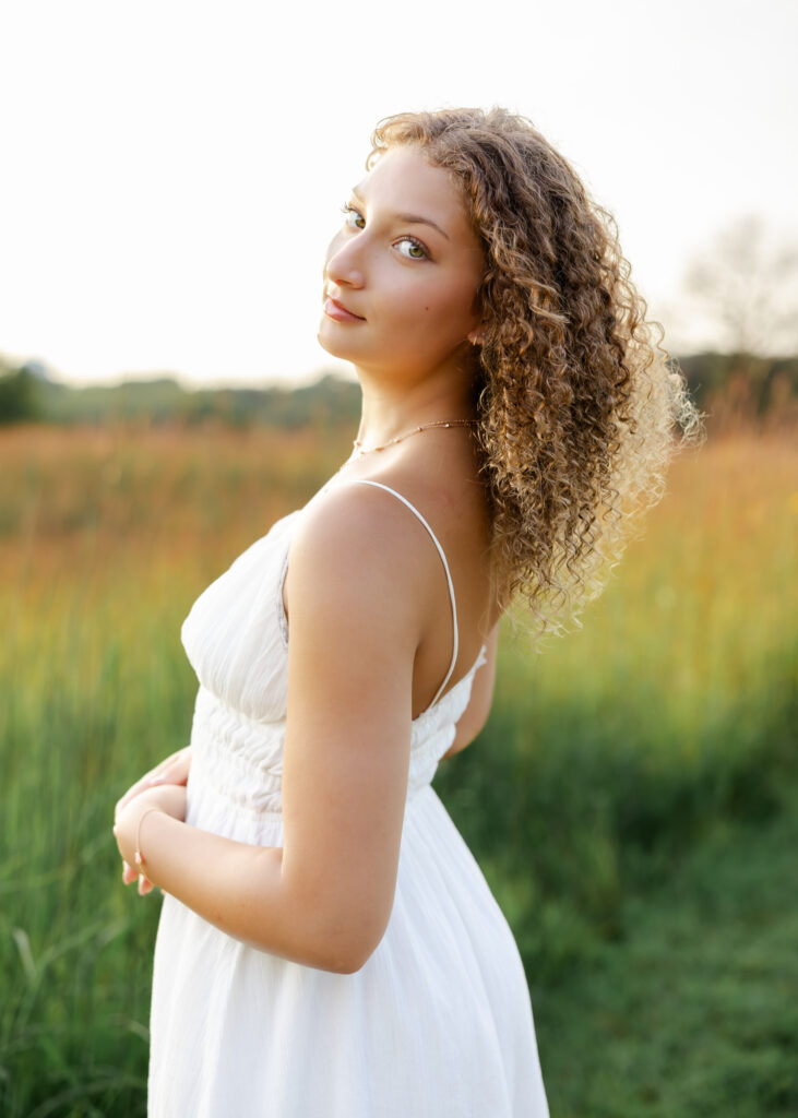 girl in long white dress and brown curly hair poses at richardson nature center for her wayzata senior photos.