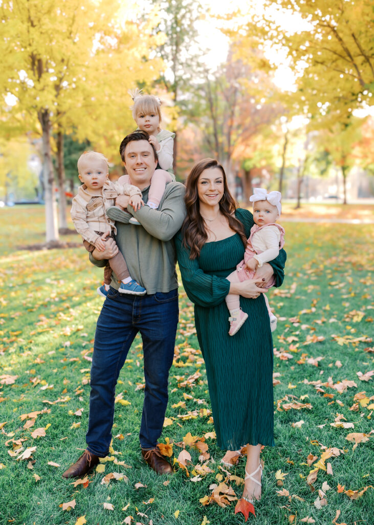 family of 5 with 3 little kids pose in the fall foliage at gold medal park for their minneapolis family photography session
