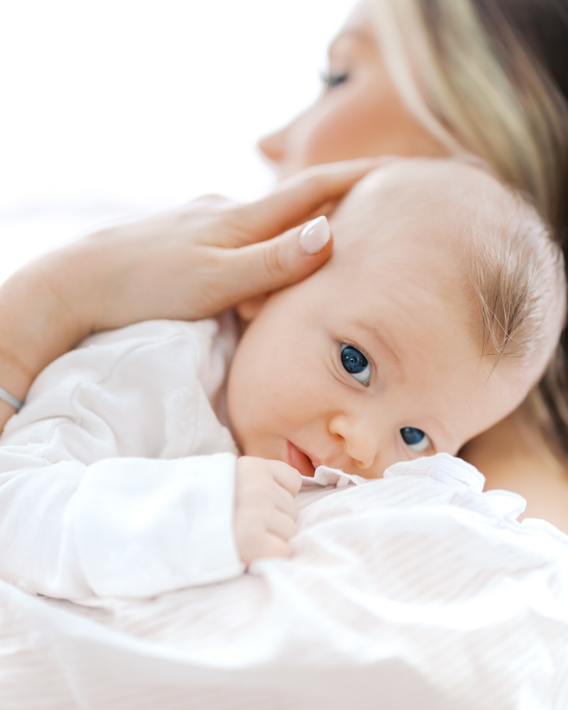 close-up of mom holding newborn baby boy in a sweet bonnet in their edina living room during their edina newborn photography session