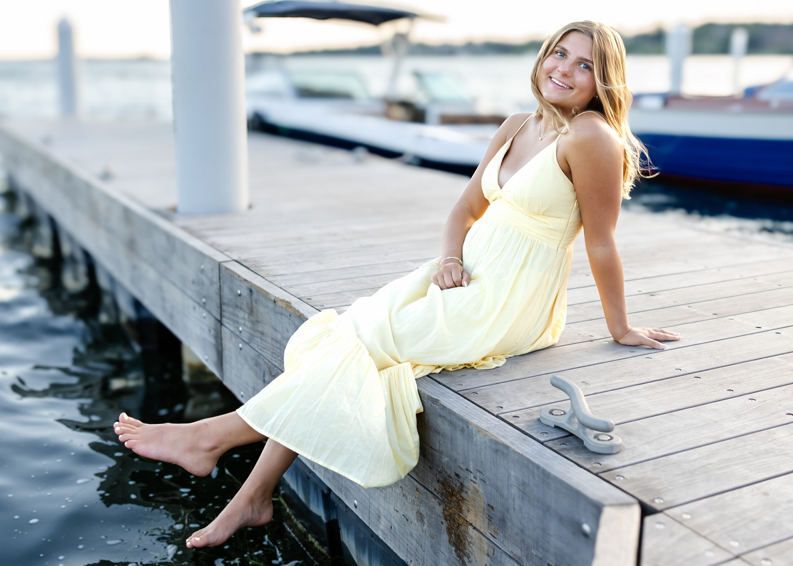 girl in long yellow maxi sits on docks downtown wayzata for her minneapolis senior pictures