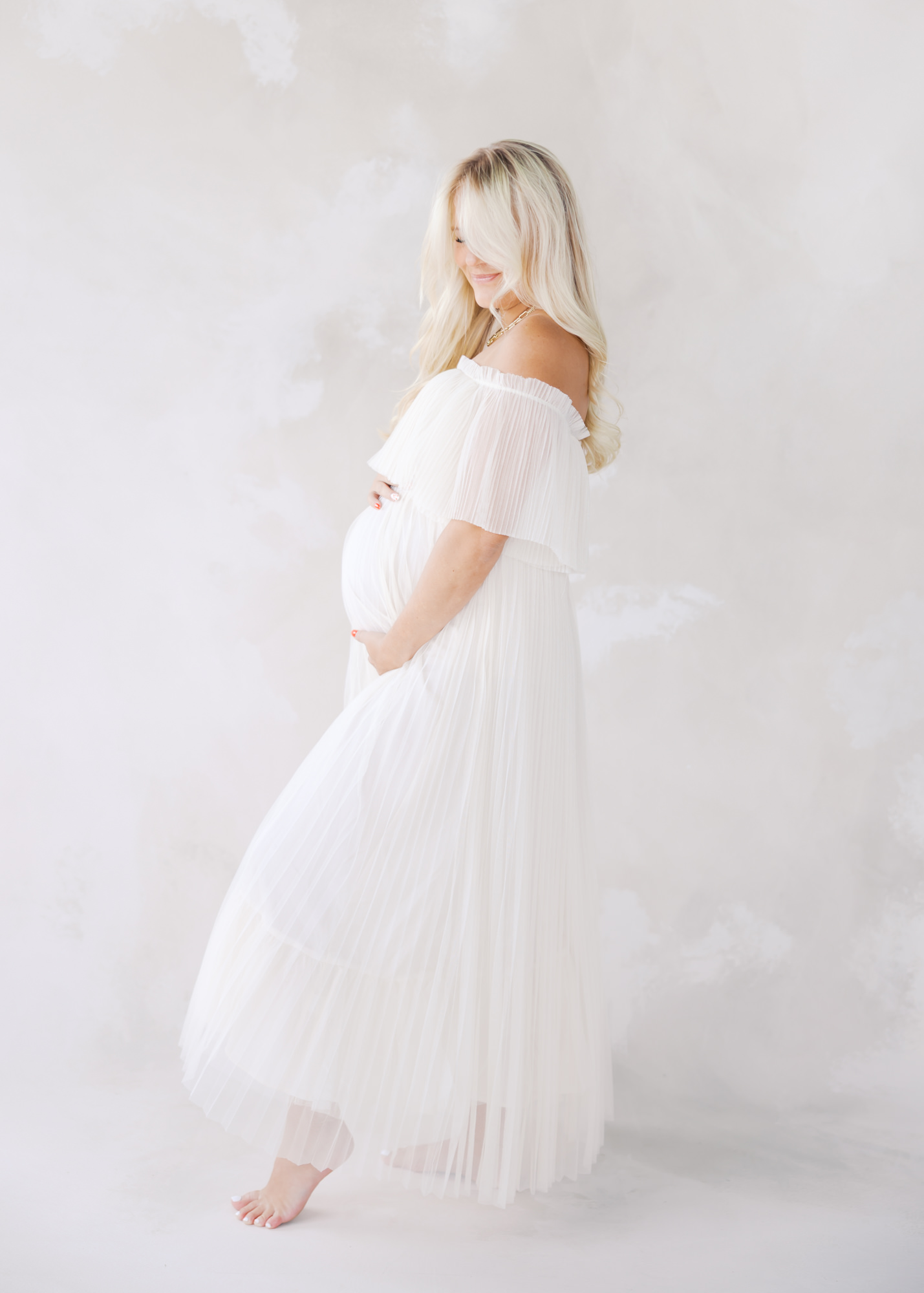 woman in white tulle maternity gown poses elegantly in a minneapolis studio for her maternity photos