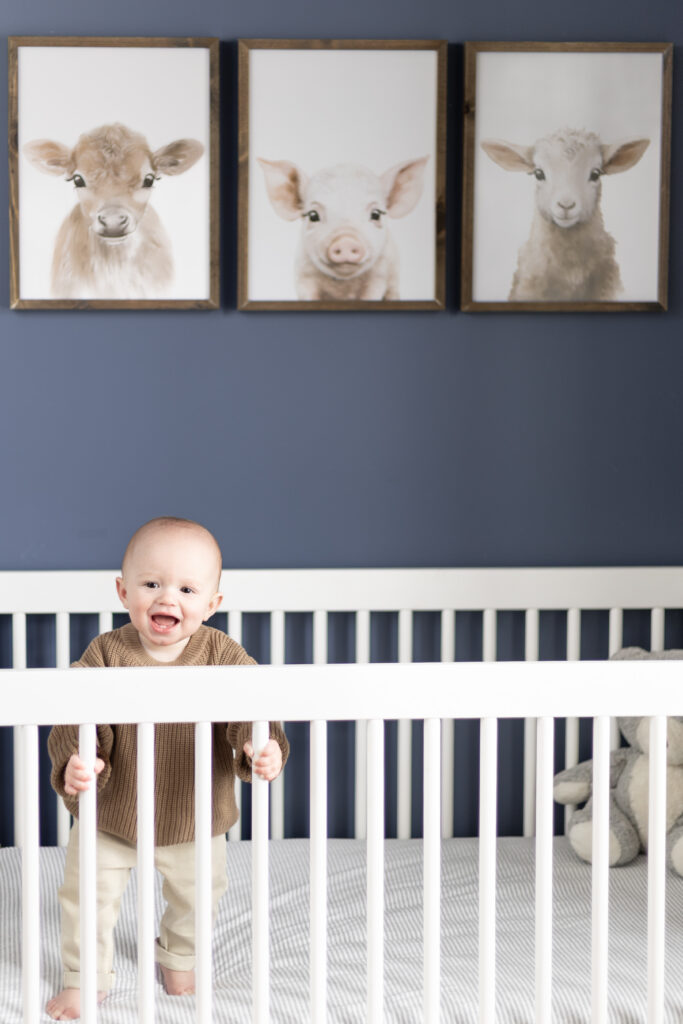 8 month old boy stands in his crib and smiles during his edina family photography session with angela watts
