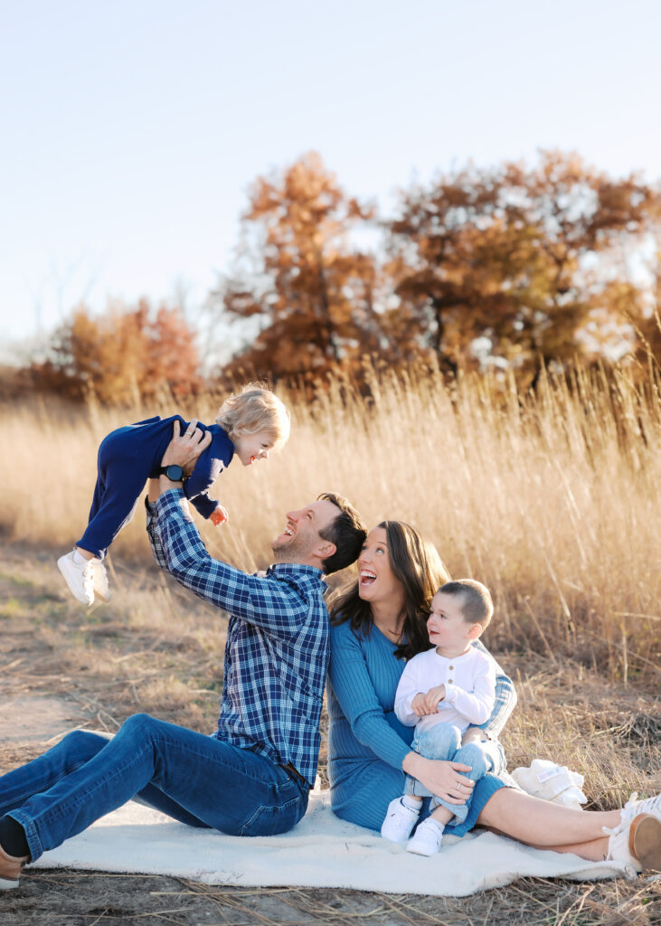 family of four sit on a blanket with golden field behind them during their minneapolis family photography session