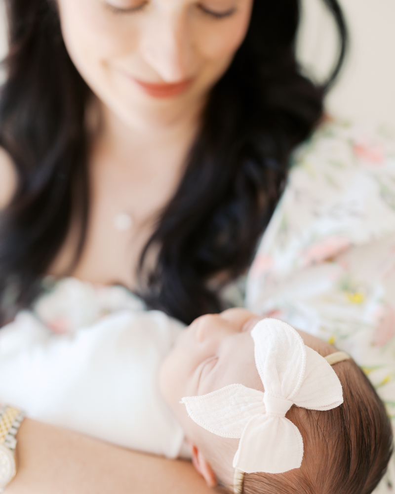 elegant woman with dark hair holds newborn baby girl wearing pink bow in an up-close image during their minneapolis newborn photography session