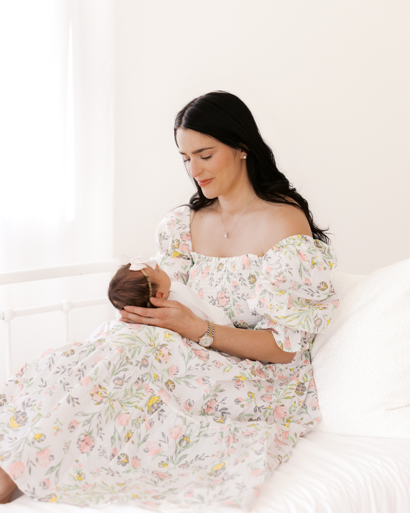 Mom holds newborn baby girl on her lap surrounded by windows and white walls during their minneapolis newborn photoshoot.