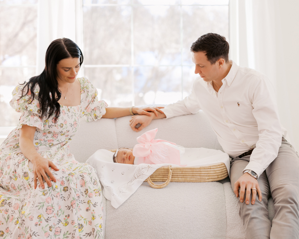 Mom and dad sit on large sofa in a light-filled studio for their minneapolis newborn photography session with angela watts.